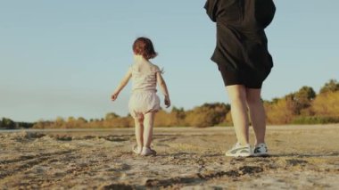 Genç bir çocuk kumlu bir plajı neşeyle keşfederken bir yetişkin, sakin ve güzel bir anı yakalıyor.