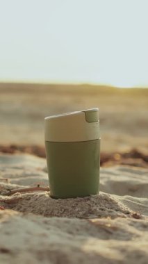 Yumuşak kumların üzerindeki parlak bir seyahat kupası çarpıcı bir günbatımında sükunet ve çevre dostu bir tarzı somutlaştırır. Dikey 