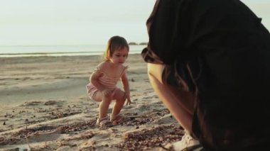 Küçük bir kız neşeyle sıcak kumu keşfeder yanında şefkatli bir gardiyanla güzel, sakin bir sahilde.