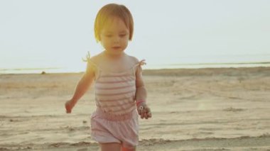 Neşeli ve mutlu bir bebek kumlu sahilde mutlu bir şekilde geziniyor. Deniz kenarında güneşli ve aydınlık bir günün tadını çıkarıyor.