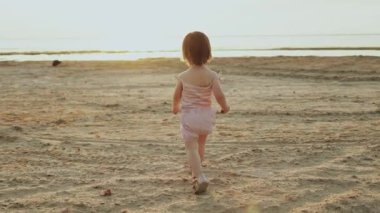 Coşkulu bir çocuk, sakin kumlu bir plajda büyüleyici güzellikteki bir gün batımına doğru neşeyle yürüyor.