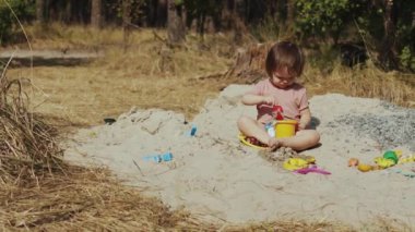 Neşeli bir çocuk neşeli doğayla çevrili güneşli kumlu bir alanda canlı, renkli bir dizi oyuncakla mutlu mesut meşgul olur.