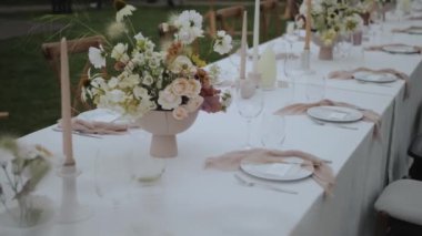 Zarif bir şekilde düzenlenmiş açık hava yemek masası. Canlı çiçekler ve sofistike masa düzenleriyle süslenmiş.