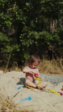 Genç bir çocuk, doğayla çevrili kumlu güzel bir sahilde renkli ve eğlenceli oyuncaklarla oynamaktan mutlu olur. Dikey video. 