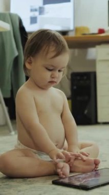 Meraklı küçük bir çocuk renkli bir tableti mutlulukla keşfediyor. İlk dijital nişan yeteneklerini sergiliyor. Dikey video.