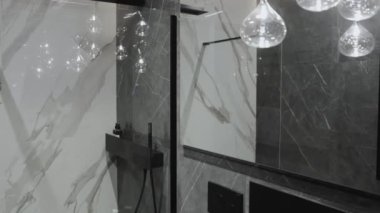 Bu modern banyo, modaya uygun, şık cazibesini arttırmak için çarpıcı mermer duvarlar ve parlak armatürler barındırıyor.