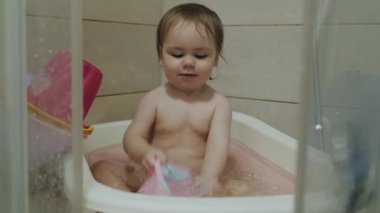 Neşeli bir bebek küvette mutlu bir şekilde sıçrıyor, neşeyle dolu neşeli su anlarının tadını çıkarıyor.