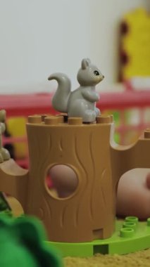 Dikey video. Tuhaf ve tapılası gri bir sincap heykeli neşeli bir ortamda oyuncak bir ağacın kütüğüne tünemiş.