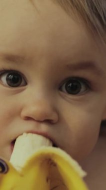 Dikey video. Mutlu bir çocuk, parlak sarı bir muzdan zevk alır, çocukluk sevinçlerini ve sağlıklı beslenmenin değerini vurgular.