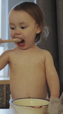 Neşeli küçük bir çocuk yemeğiyle mutlu bir şekilde oynuyor, yemek zamanının basit zevklerini neşeyle sergiliyor. Dikey video.