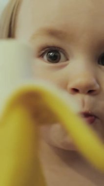 Çocukluk masumiyetini ve neşesini gözler önüne seren, keyifli, muz yiyen bir çocuğun büyüleyici yakın çekimi. Dikey video.