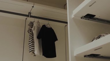 Zarif bir şekilde asılmış siyah ve çizgili tişörtler içeren modern bir dolap tasarımı, minimalist bir stil sergiliyor.