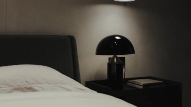 Bu şık, modern yatak odasında zarif bir yatak ve yumuşak, davetkar bir ışık saçan siyah bir lamba sergileniyor.