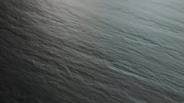 Okyanus yüzeyinin sakin ve sakin görüntüsü hafif dalgalar ve suda güzel yansımalar sergiliyor.