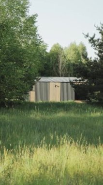 Büyüleyici bir bahçe kulübesi, berrak gökyüzünün altındaki gür çimlerin ve ağaçların olduğu verimli bir alanda huzur içinde yatıyor. Dikey video.