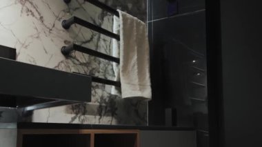 Bu şık banyoda güzel mermer duvarlar sergileniyor. Parlak, modern eşyalar ve yumuşak bir havlu asılı.