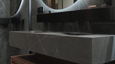 Bu zarif ve modern banyo lavabosu, dokulu bir yüzey ve büyük yuvarlak bir ayna ile vurgulanmış şık bir minimalist tasarım sergiliyor.