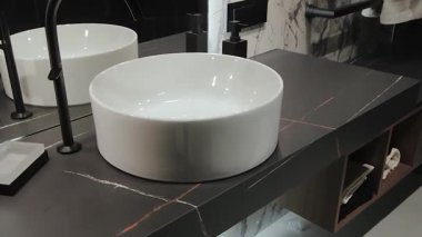 Burası şık bir banyo. Çağdaş bir tezgahın üzerine güzel yerleştirilmiş parlak, yuvarlak bir lavabo var.