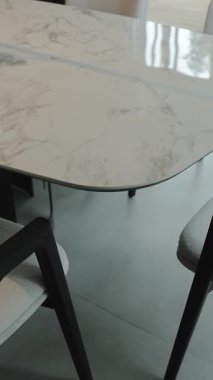 Modern sandalyelerle birleştirilmiş mermer bir yemek masasının yakın çekimi. Parlak ve ferah bir oturma odasında. Dikey video