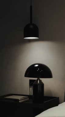 Bu şık, modern yatak odasında zarif bir yatak ve yumuşak, davetkar bir ışık saçan siyah bir lamba sergileniyor.