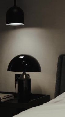 Parlak ve şık bir siyah lamba, çağdaş bir yatak odası ortamındaki bir komodinin üzerine güzelce yerleştirilmiş.