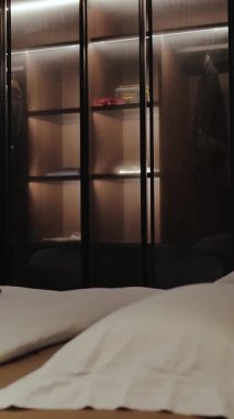  Dikey ekran: Şık ve modern bir gardırop, şık LED ışıklandırmayla renklendirilmiş hoş kıyafetler sergiliyor.