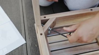 Bir kadının, evinin yakınındaki ahşap mobilyaları bir İngiliz anahtarı ile monte ederken çekilmiş yakın çekimi.