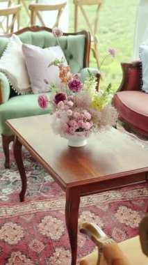 Dikey çekim: Zarif ve güzel düzenlenmiş bir çiçek süsü şık bir sehpanın üzerine konmuş samimi bir sehpada.