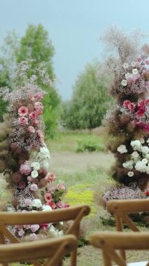 Çiçeklerle süslenmiş düğün kemerinin yakın çekimi. Doğada ayarlanmış güzel çiçek düzenlemeleri. Dikey video 4k