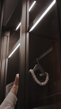 Dolaptan elbise çıkaran bir kadının elinin yakın çekimi. Modern moda eşyaları ve aksesuarları etkili bir şekilde gösteren zarif dolap tasarımı. Dikey video