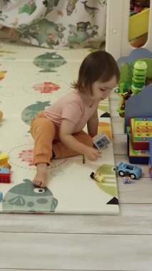 Toddler renkli bloklar ve oyuncaklarla oynuyor. Yerde oturuyor, gelişmeyi ve hayal gücünü destekliyor. Dikey video. 4k