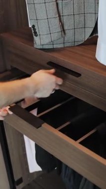 Düzgün katlanmış ve organize edilmiş kıyafetlere ulaşmak için gardırop çekmecesini açan bir adamın eli. Dikey video 4k