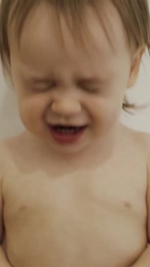 Bebek gülüyor, beyaz bir duvarın önünde duruyor, neşe, duygular, güzel bir kız. Dikey çekim. 4k