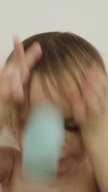 Neşeli bir çocuk beyaz bir duvarda renkli fincanlarla oyuncaklarla oynar, çocuk güler ve sevinir. Dikey çekim 4k