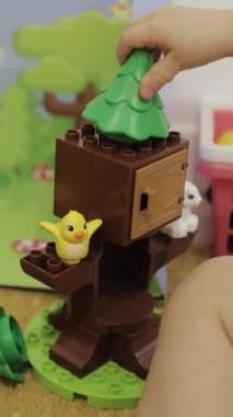 Bir çocuk neşe içinde renkli blokları birleştiriyor, canlı bir ağaç sahnesi yaratıyor, hayvanlarla birlikte. Dikey çekim 4K