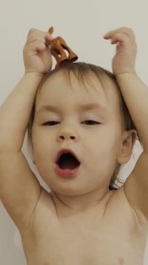 Bebek bezli mutlu bir bebek, neşeli bir şekilde renkli bir oyuncakla oynayıp parlak bir odada beyaz bir arka planda kafasına takar. Dikey çekim. - Evet. Yüksek kalite 4k görüntü