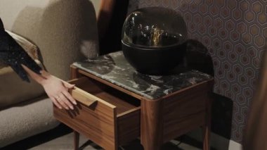 Bir kadın, modern bir komodinin çekmecesini açıyor. Güzel mermer kapaklı şık bir komodin. Ahşap çekmece ve cam lamba. - Evet. Yüksek kalite 4k görüntü