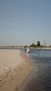 Dikey ekran: Anne ve çocuk nehre bakıyor, yazın kumsalda yürüyor. Sahilde aile eğlencesi. Aile günü neşe, macera ve beraberlikle dolu. Huzurlu bir günün tadını çıkar