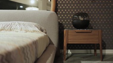 Modern yataklı şık bir yatak odası, ahşap bir komodin, şık bir dekor ve sıcak bir atmosfer için zarif elementler. Yüksek kalite 4k görüntü