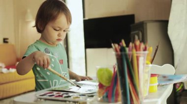 Yaratıcı çocuk evinde farklı renklerde bir boya fırçası ve parlak bir odada masasında dururken malzemeler çiziyor. Yüksek kalite 4k görüntü