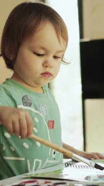  Dikey ekran: Bir kız evinde, parlak bir odada, masasında fırçayla resim yapıyor, renkli boya ve fırçalar kullanarak sanatsal tarafını mutlulukla keşfediyor. Yüksek kalite 4k görüntü