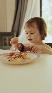 Dikey ekran: Sevimli ve neşeli bir çocuk mutlu bir şekilde bir tabak makarna ve taze et yiyor.