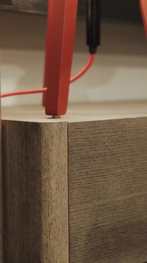 Dikey. Lambalı ahşap bir komodinin yakın plan çekiminde kamera geri çekiliyor. Parlak kırmızı aksanlı şık ahşap mobilyalar modern iç tasarım eğilimlerini mükemmel bir şekilde gösteriyor. Yüksek kalite 4k