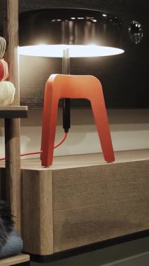 Kırmızı ve siyah bir lamba rahat bir iç mekanı aydınlatır ve ahşap bir komodinin üzerinde durur. Ev dekorasyonu için mükemmeldir. Dikey video. Yüksek kalite 4k görüntü