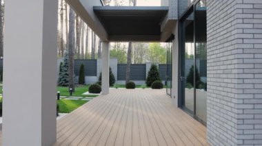 Minimalist bahçede pahalı bir evin yanındaki ahşap teras. Modern açık alan. Ahşap zemini, kafes çatısı, geniş penceresi olan teras. Kamera sorunsuz hareket ediyor. Lüks bir ev. Gün batımı. Yüksek kalite 4k görüntü