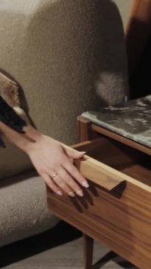 Dikey ekran: Bir kadın modern bir komodinin çekmecesini açar. Ağır çekim. Güzel mermer kapaklı şık bir komodin. Ahşap çekmece ve cam lamba. - Evet. Yüksek kalite 4k görüntü