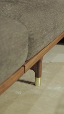 Dikey video. Modern bir kanepe, gri çerçeveli, tahta bacaklı ve altın elementli, modern tasarımın konfor ve estetiğinin mükemmel bir kombinasyonunu gösteren. Yüksek kalite 4k
