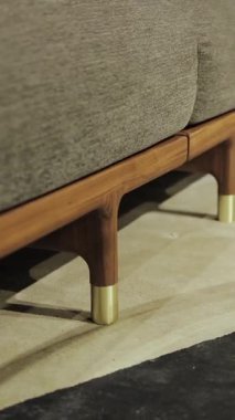 Dikey video. Tahta yatak bacaklarına yakın çekim. Bu şık oturma odasında zarif ve modern bir sehpa ve yumuşak ve rahat bir kanepe var. Yüksek kalite 4k görüntü