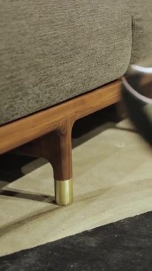 Dikey video. Tahta bacaklı bir kanepenin yakın çekimi. Cam kapaklı şık bir sehpa ve ev için ahşap taban. Kimse vurulmayacak. Yüksek kalite 4k görüntü