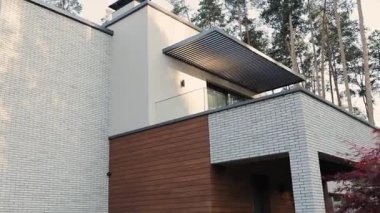 Balkonlu modern mimari tuğla ev. İki katlı özel bir ev, zarif bir şekilde yemyeşil ağaçlar ve doğa ile çevrili. Yüksek kalite 4k görüntü